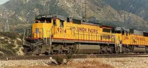 A yellow train is on the tracks near some mountains.