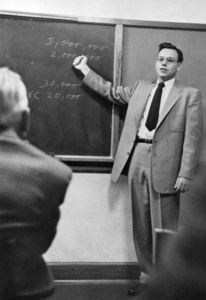 A man in a suit and tie is writing on the chalkboard