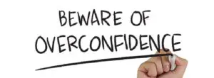 A hand writing on paper that says beware of overconfidence.