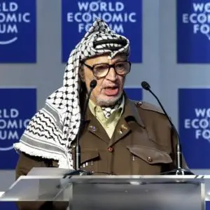 A man in a keffiyeh speaking at a podium.