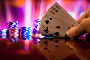 A hand holding four aces in front of a casino table.