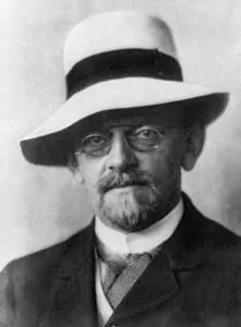 A man with glasses and a hat is wearing a suit.