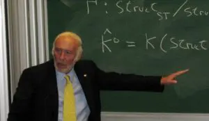 A man in suit and tie pointing at a chalkboard.