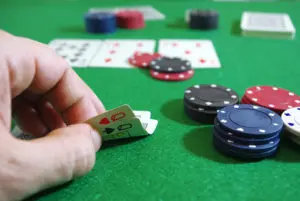 A person holding two cards over chips on a green table.