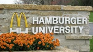 A sign that says hamburger university and some flowers.