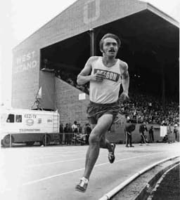 A man running on the track in front of an audience.