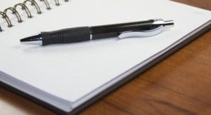 A pen and notebook on top of a wooden table.